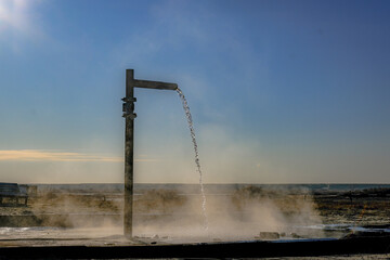 A faucet with warm water flowing to the ground on a frosty day