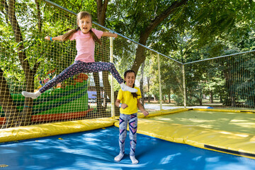 two girls jumping on a trampoline on a summer day.