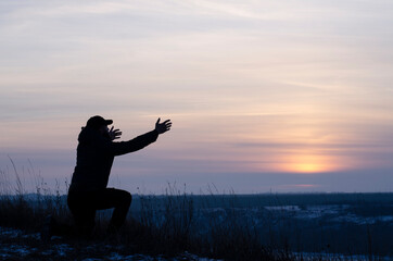 Pray. Repentance. Silhouetted men on a background of blue sky and sunset. Kneeling Prayer to God. Glorification. Christian - obrazy, fototapety, plakaty