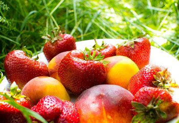Strawberries and peaches on a plate on the green grass. Delicious and fresh summer fruits. Healthy vegetarian food with vitamins.