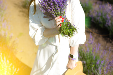 Girl in white linen dress with lavender bouquet and straw hat walking in Beautiful purple lavender flowers on the summer field. Warm and inspiration concept. Wanderlust and traveling.