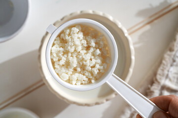 Kefir grains in a white strainer above a bowl of fresh milk