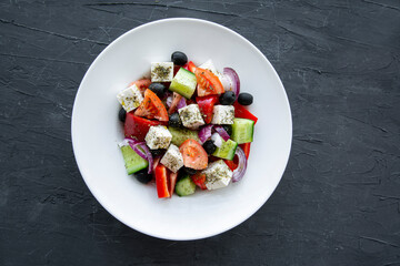 Fresh tasty greek salad on black stone concrete background, top view.