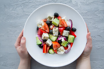 Tasty greek salad, top view. Female hands hold a plate. 