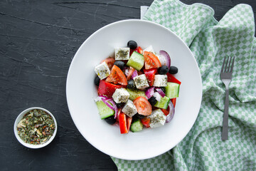 Tasty greek salad with fresh vegetables on black stone background, top view. 
