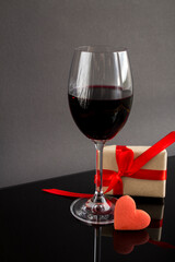 Wineglass with red wine, gift box and red heart shaped cookie on the dark  background. Close-up.