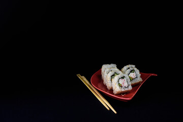 sushi rolls on a red saucer in the form of a fan on a black background of a chopstick