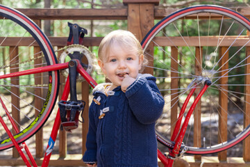 A curious infant is seen posing for the camera with curly blonde hair and blue coat exploring...