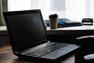 Fototapeta premium Laptop on the table. Window in the background. Work from home. Office equipment in the workplace. Conceptual image of office work.