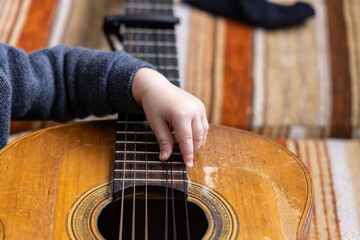 Fototapeta premium Closeup and detailed view on the hand of a toddler playing the strings of a guitar. Curious young boy learning a musical instrument with copy space.