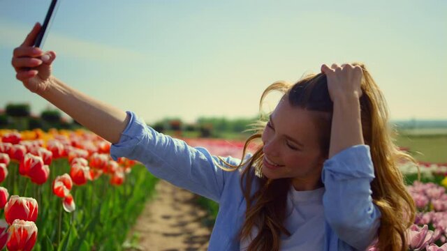 Pretty woman flirting online in spring flower garden. Smiling girl making selfie