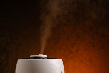 Modern humidifier generates vapor on orange background. Steam from working air purifier.