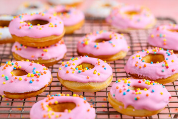 Pink vanilla mini donuts with sprinkles on a metal grill. Close-up. Selective focus 