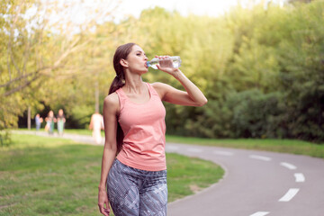 Athletic woman standing running track in summer park drink water after running exercises