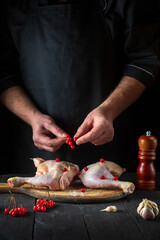 The chef prepares raw chicken legs in the restaurant kitchen. The cook puts red viburnum berries on a chicken leg before baking. National dish