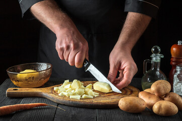The chef cuts raw potatoes into pieces with a knife before preparing breakfast or dinner. Close-up of a cook hands while working in a restaurant kitchen.