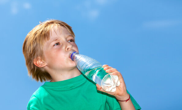 little boy drinking water from a bottle against a blue sky