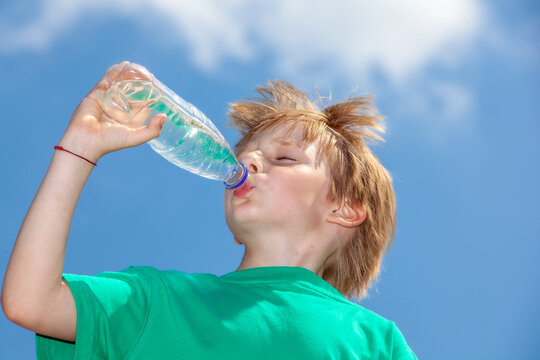 little boy drinking water from a bottle against a blue sky
