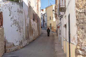 Rear view of an elderly man in a beret walking alone along an empty street in a town.
