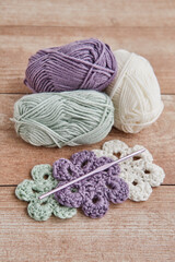 Skeins of yarn, colorful knitted flowers and knitting hook on wooden table.
