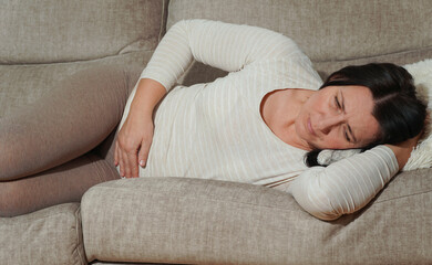 Middle aged mature woman suffering from stomach ache at home. Abdominal pain, food poisoning,...