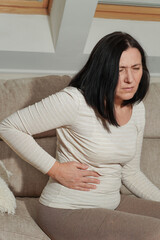 Middle aged mature woman suffering from backache and flank pain at home. Sickness, ilness, sadness...
