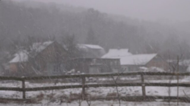 Snow is falling on a blurred background of houses.