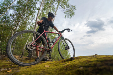 Cyclist in a helmet with a bike standing on the edge of a cliff in the forest. Active sport...