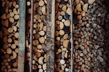 Wood natural sawn logs as background. Stacked wall wood logs. Stacked of firewood arranged with cracks on cross section. Textured abstract background.