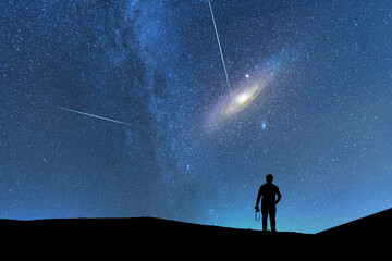 Silhouette of a person on the hill in starry night sky.  Bright andromeda galaxy and meteors behind...
