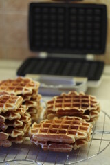 Freshly made homemade Viennese waffles on a mesh rack. Open waffle iron in the background.