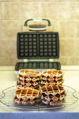 Freshly made homemade Viennese waffles on a mesh rack. Open waffle iron in the background.