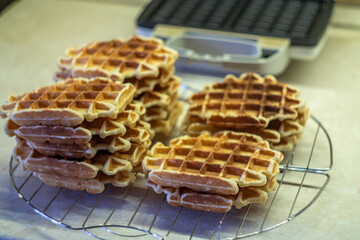 Freshly made homemade Viennese waffles on a mesh rack. Open waffle iron in the background.