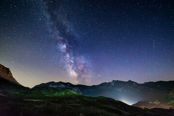 Fototapeta na wymiar the Milky way galaxy and stars over the Italian French Alps. Night sky on majestic snowcapped mountains and glaciers. Meteor shower on the right