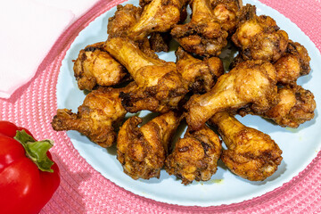 Appetizing chicken wings and red pepper on the table. Delicious fried chicken wings on a blue plate