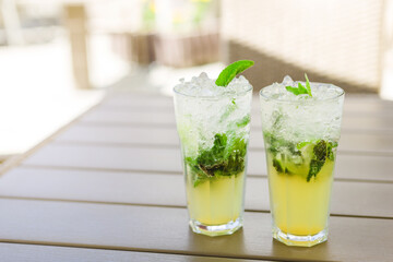 Two glasses of Lemonade or mojito cocktail with lemon and mint, cool refreshing drink or beverage, outdoor. Cold detox water with ice, copy space, summer day.