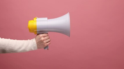 Profile side view closeup of woman hand holding megaphone, announcing of advertisement or protesting. Indoor studio shot isolated on pink background.