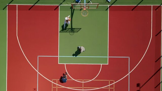 Aerial view of two young male friends playing basketball on court outdoors and cameraman filming video
