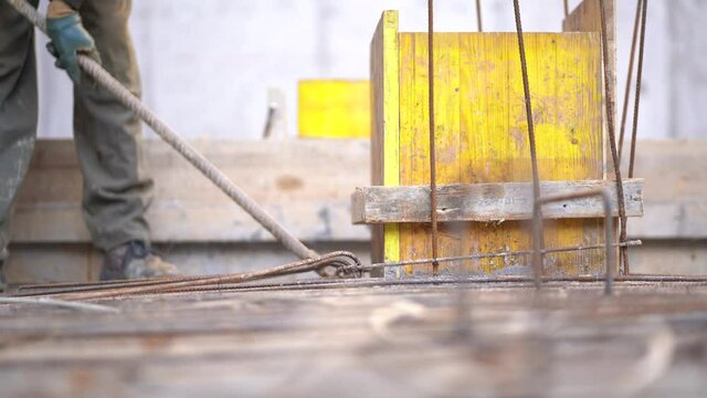 Worker twisting reinforcement steel rebars to strengthen building foundation at a construction site, close up static 4K
