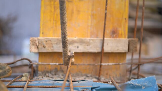 Worker twisting reinforcement steel rebars to strengthen building foundation at a construction site, close up static 4K