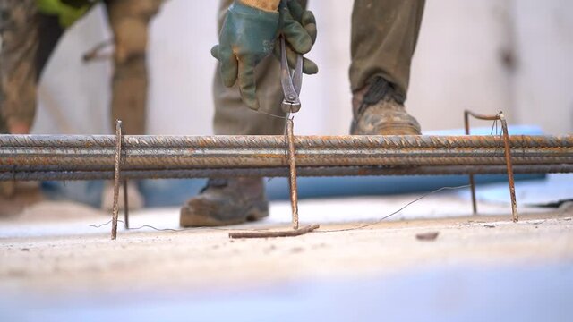 Caucasian laborer using lineman's pliers to tie steel rebars together in a construction site, close up static
