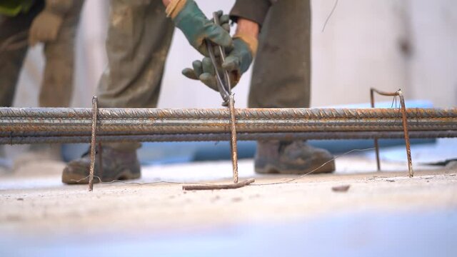 Worker tying metal reinforcement rebars with steel wire using lineman's pliers at construction site, close up static
