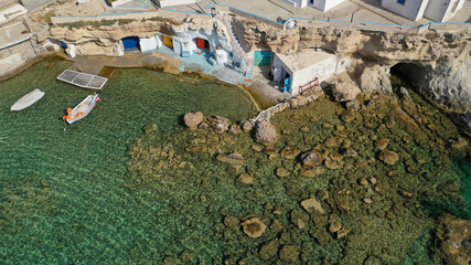 Aerial drone photo of picturesque small fishing harbour of Mandrakia with traditional boat houses called syrmata and anchored fishing boats, Milos island, Cyclades, Greece