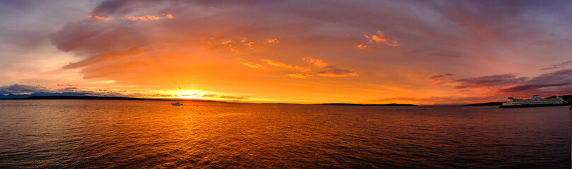 Obraz premium A view of the Olympic Mountains in the background and Puget Sound in the foreground at sunset with a colorful sky and clouds