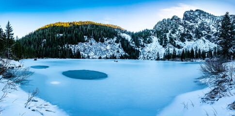 A panoramic view of a snow and ice covered Lake Heather with snow covered trees and hills in the background