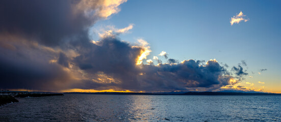 A panoramic view of a sunset over Puget Sound with tall colorful clouds in the sky