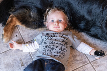 High angle shot of a three year old boy, full of mischief, lying on a tiled kitchen floor resting head on stomach of large family dog with copy space.