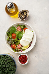 Salad with green leaves, lettuce, spinach, cherry tomatoes, mozzarella, olive oil, chilli pepper, lime juice on grey stone surface, top view