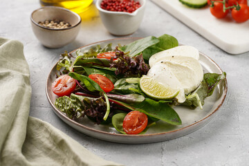 Salad with green leaves, lettuce, spinach, cherry tomatoes, mozzarella, olive oil, chilli pepper, lime juice on grey stone surface