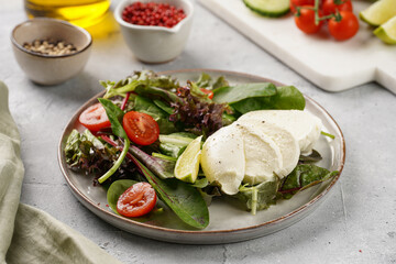 Salad with green leaves, lettuce, spinach, cherry tomatoes, mozzarella, olive oil, chilli pepper, lime juice on grey stone surface